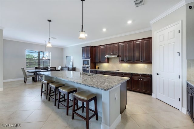 kitchen featuring a center island with sink, crown molding, light stone countertops, and pendant lighting