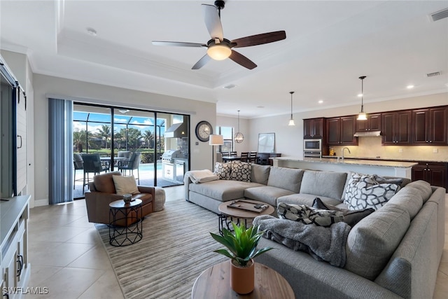 living room featuring ceiling fan, a tray ceiling, ornamental molding, light tile patterned flooring, and sink