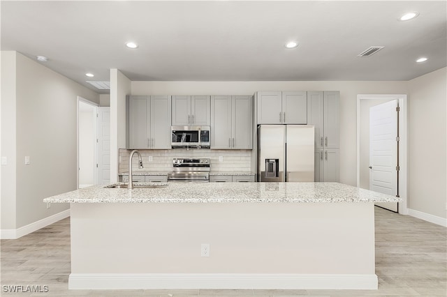 kitchen featuring a center island with sink, sink, light stone countertops, and stainless steel appliances