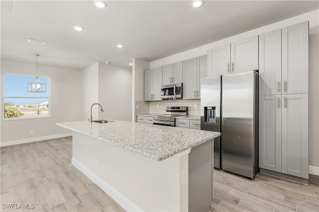 kitchen with a center island with sink, light stone countertops, pendant lighting, light hardwood / wood-style floors, and stainless steel appliances