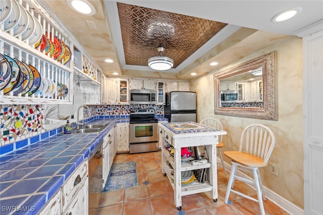 kitchen with white cabinets, a raised ceiling, tile countertops, sink, and stainless steel appliances