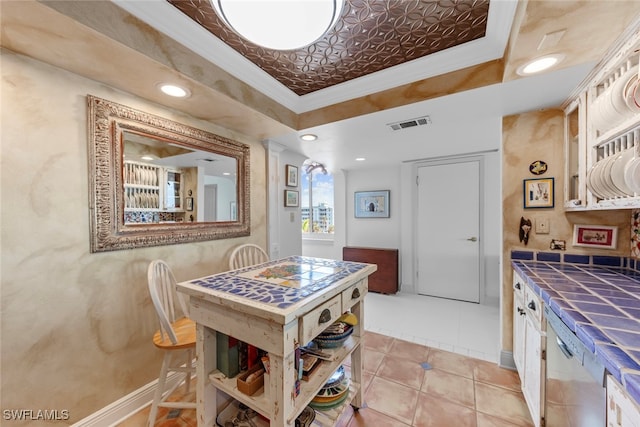 kitchen with tile countertops, ornamental molding, light tile patterned flooring, and a tray ceiling