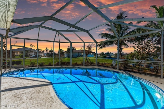 pool at dusk with a patio area, a lanai, and a lawn