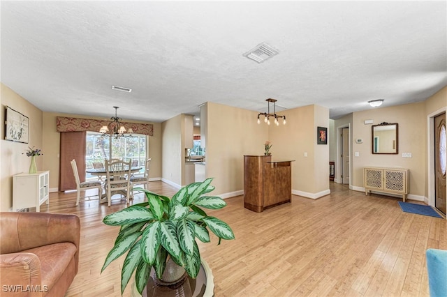 living room featuring a textured ceiling, a chandelier, and light wood-type flooring