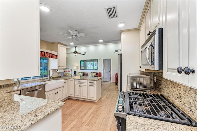 kitchen with light stone countertops, light hardwood / wood-style flooring, kitchen peninsula, and stainless steel appliances