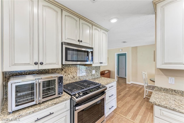 kitchen featuring light stone countertops, appliances with stainless steel finishes, light hardwood / wood-style floors, and tasteful backsplash