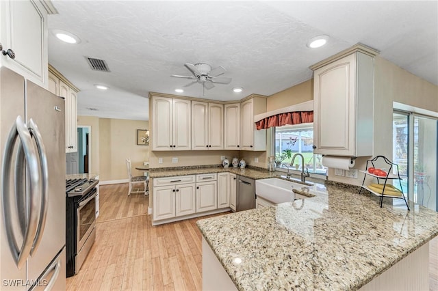 kitchen with kitchen peninsula, stainless steel appliances, sink, light stone countertops, and light hardwood / wood-style floors