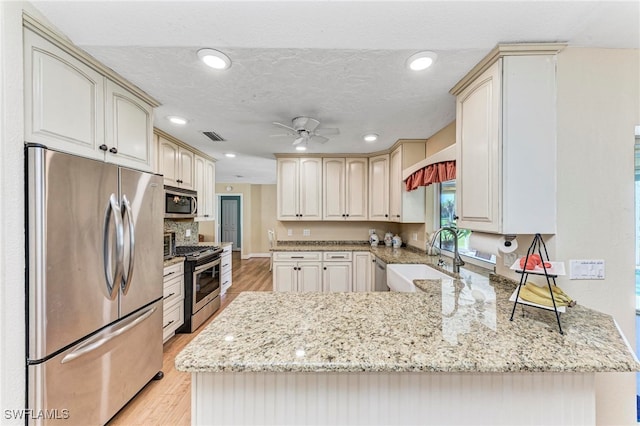 kitchen with light hardwood / wood-style flooring, kitchen peninsula, sink, appliances with stainless steel finishes, and ceiling fan