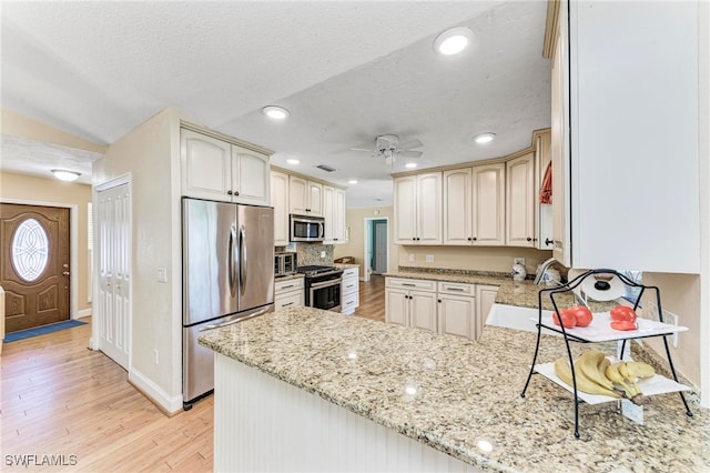 kitchen with kitchen peninsula, appliances with stainless steel finishes, a textured ceiling, light stone countertops, and light wood-type flooring