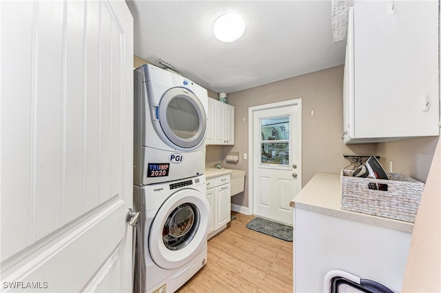 clothes washing area with light hardwood / wood-style flooring, sink, stacked washer / dryer, a textured ceiling, and cabinets