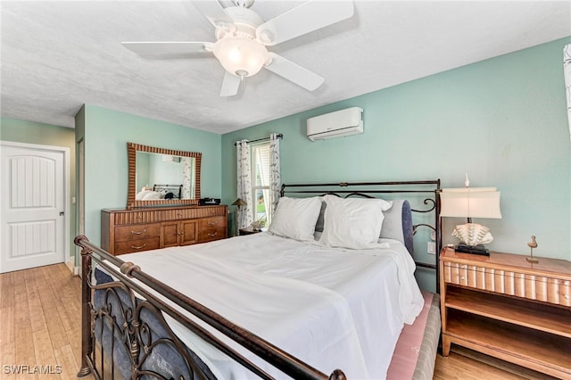 bedroom featuring a wall unit AC, a textured ceiling, light wood-type flooring, and ceiling fan