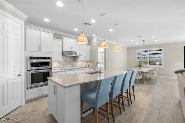 kitchen with sink, double oven, decorative light fixtures, a kitchen island with sink, and white cabinets