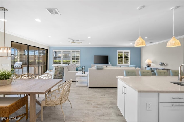 kitchen with ornamental molding, ceiling fan, sink, pendant lighting, and white cabinetry