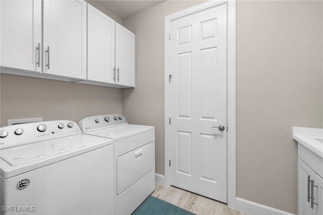 laundry room featuring washer and dryer, cabinets, and light wood-type flooring