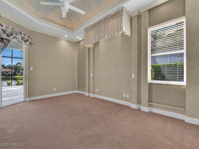 carpeted empty room with plenty of natural light, ceiling fan, ornamental molding, and a tray ceiling