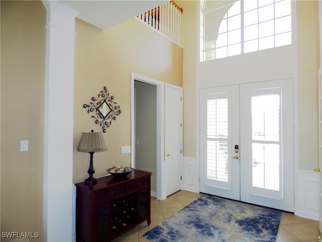 foyer featuring a high ceiling, french doors, light tile patterned floors, and ornate columns