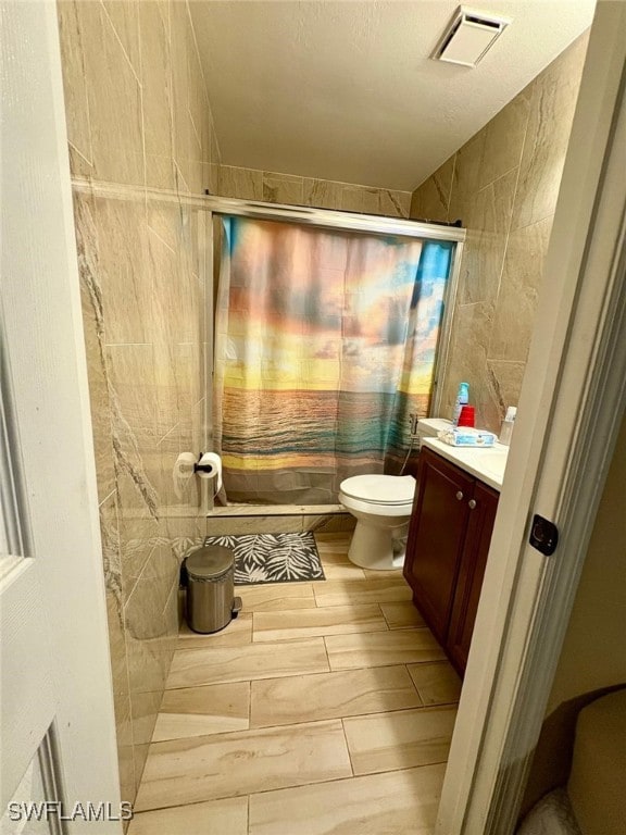 full bathroom featuring vanity, shower / tub combo with curtain, toilet, and tile walls