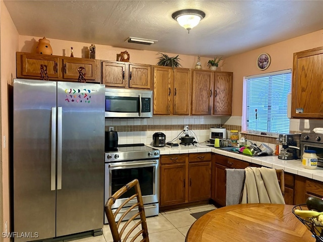 kitchen with appliances with stainless steel finishes, sink, backsplash, tile counters, and light tile patterned floors