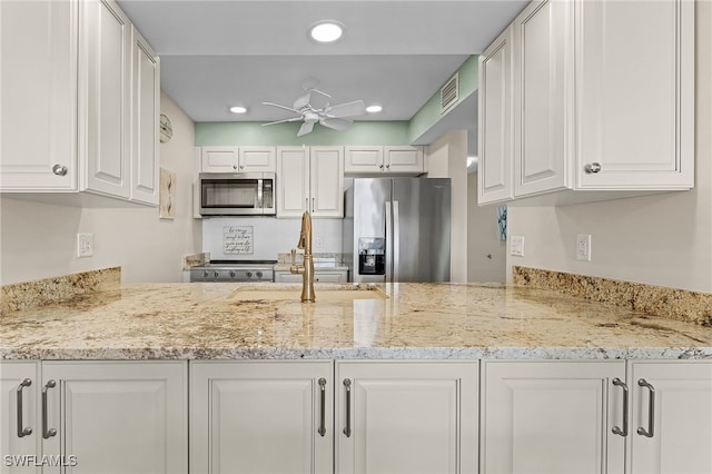 kitchen with white cabinets, ceiling fan, appliances with stainless steel finishes, light stone countertops, and sink