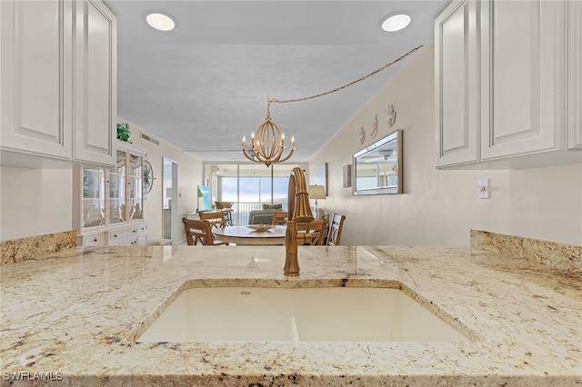 kitchen featuring sink, white cabinets, light stone counters, and an inviting chandelier