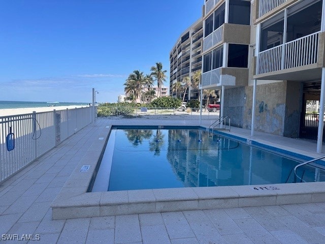 view of swimming pool featuring a patio area, a water view, and a view of the beach