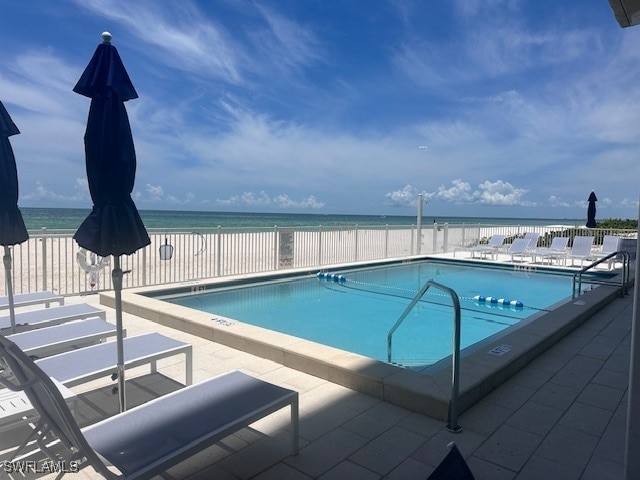 view of pool with a patio, a view of the beach, and a water view