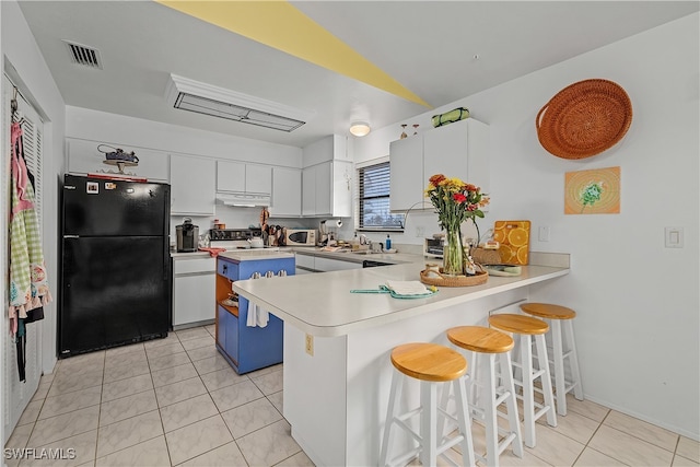 kitchen with kitchen peninsula, black fridge, light tile patterned floors, white cabinetry, and a breakfast bar area