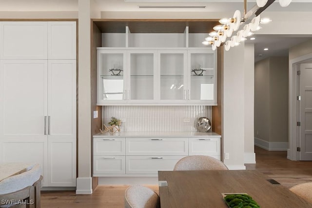 bar with light wood-type flooring, tasteful backsplash, white cabinets, a chandelier, and hanging light fixtures