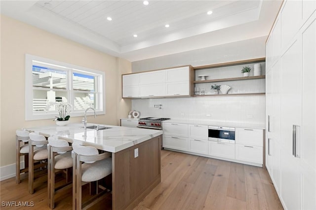 kitchen featuring sink, a raised ceiling, light stone counters, a breakfast bar, and white cabinets