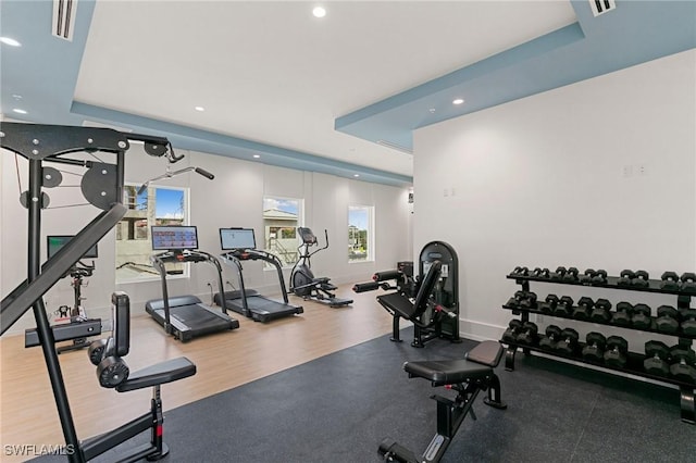 gym with hardwood / wood-style floors and a tray ceiling