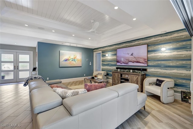 home theater with ceiling fan, a raised ceiling, light wood-type flooring, crown molding, and french doors