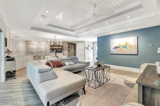 living room with crown molding, ceiling fan with notable chandelier, light wood-type flooring, and a raised ceiling