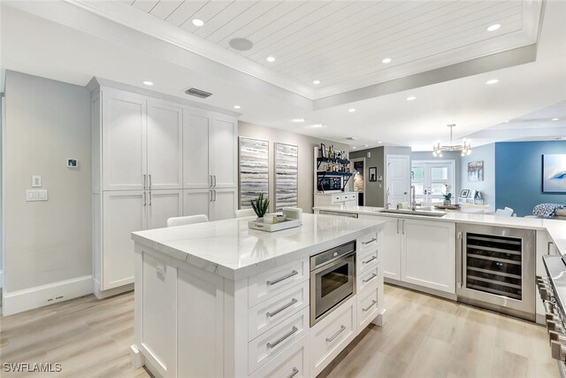 kitchen featuring white cabinets, beverage cooler, a kitchen island, light hardwood / wood-style flooring, and decorative light fixtures