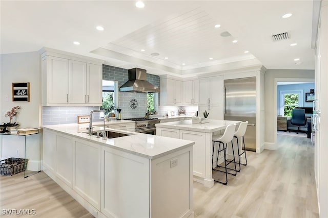 kitchen featuring a kitchen island, wall chimney range hood, high quality appliances, kitchen peninsula, and light hardwood / wood-style floors