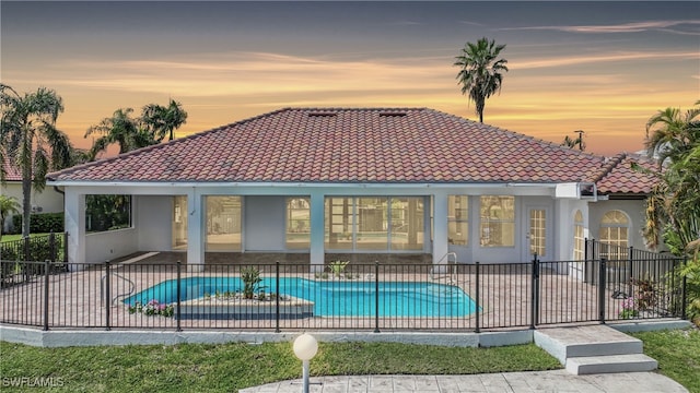 back house at dusk with a fenced in pool and a patio area