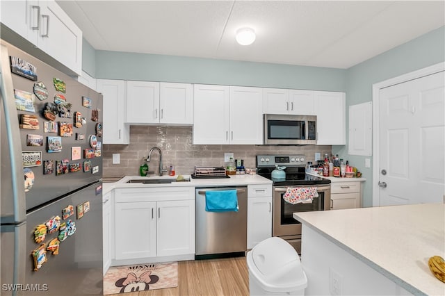 kitchen featuring decorative backsplash, sink, white cabinets, appliances with stainless steel finishes, and light hardwood / wood-style floors