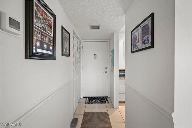 corridor with a textured ceiling and light tile patterned flooring