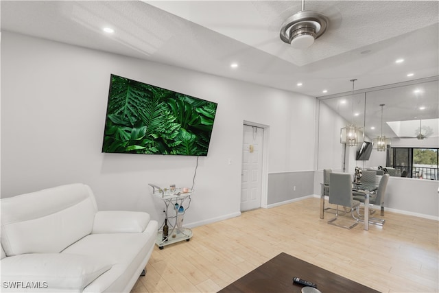 living room with ceiling fan, a textured ceiling, and light hardwood / wood-style floors