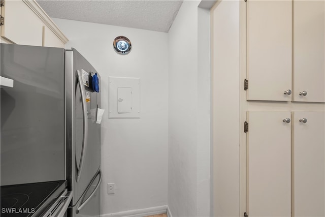 kitchen featuring electric panel, electric stove, a textured ceiling, stainless steel refrigerator, and cream cabinetry