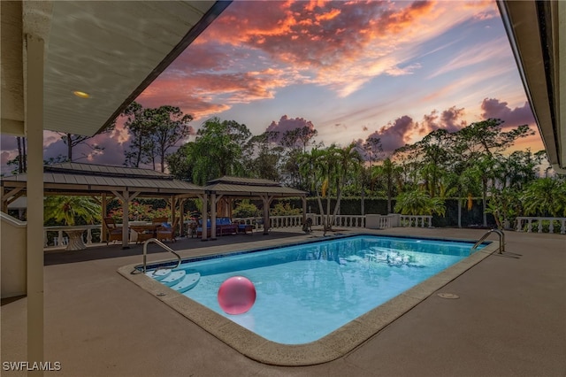 pool at dusk featuring a gazebo and a patio area