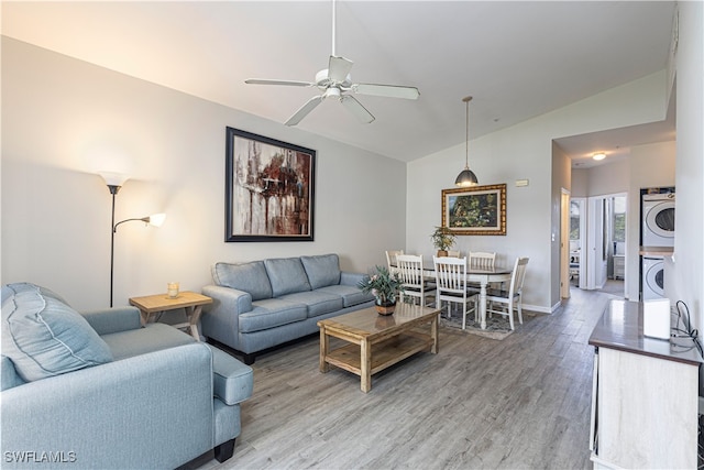 living room featuring ceiling fan, stacked washing maching and dryer, wood-type flooring, and vaulted ceiling