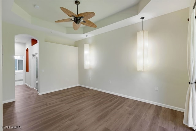 empty room featuring a raised ceiling, dark wood-type flooring, and ceiling fan