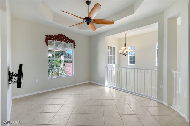 empty room featuring light tile patterned floors, ceiling fan with notable chandelier, and a raised ceiling