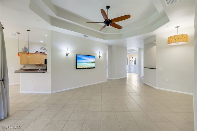 unfurnished living room with light tile patterned floors, ceiling fan, and a raised ceiling