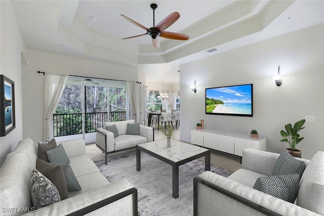 tiled living room featuring ceiling fan with notable chandelier and a tray ceiling