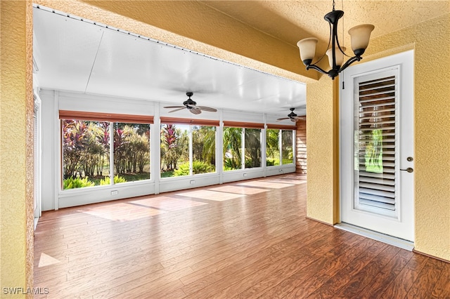 unfurnished sunroom featuring ceiling fan with notable chandelier and a healthy amount of sunlight