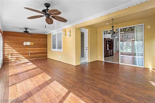 unfurnished room with dark wood-type flooring, ceiling fan, and wood walls