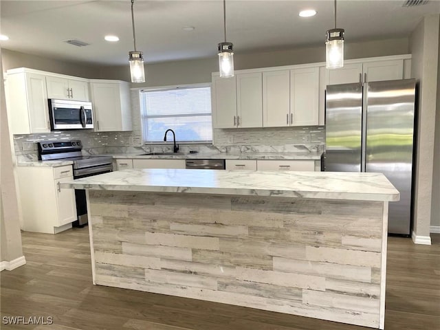 kitchen with appliances with stainless steel finishes, white cabinets, hanging light fixtures, and a center island