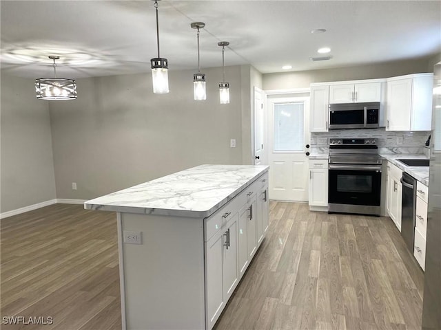 kitchen featuring white cabinets, appliances with stainless steel finishes, decorative light fixtures, a center island, and light wood-type flooring