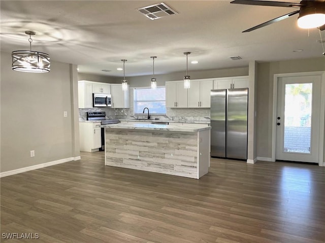 kitchen featuring appliances with stainless steel finishes, a kitchen island, decorative light fixtures, white cabinetry, and tasteful backsplash